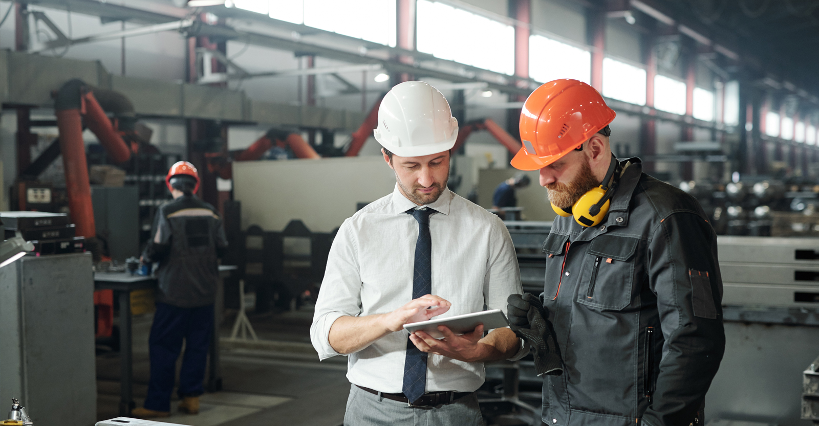 Two co-workers wearing safety gear looking at tablet in factory