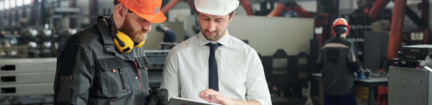 Men in factory setting looking at financials on tablet